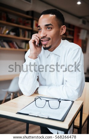 Photo of handsome african businessman sitting at the table talking by phone. Coworking.