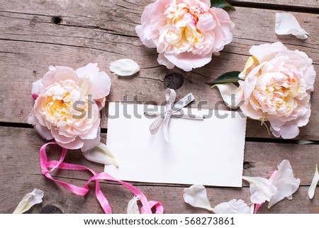 Pink peonies flowers  and empty tag on   wooden background. Flat lay. Top view with place for text. Selective focus.