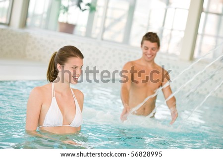 Swimming pool - young couple have fun under water stream, focus on woman in bikini