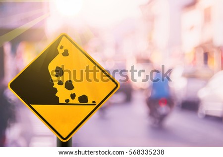 Falling stone warning traffic sign on blur road with colorful bokeh light abstract background. Copy space of travel and transportation concept. Vintage tone filter effect color style.