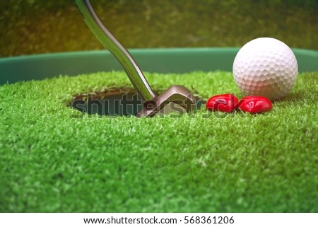 Golf ball and putter next to the hole with two hearts.
