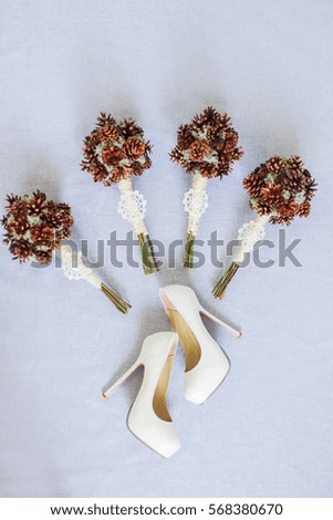 Elegant stylish bouquets made of fir-cone and cotton. White wedding shoes on grey background. Close up photo. Light fine art bridal morning preparation.