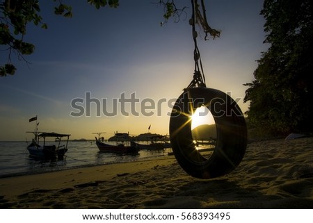 Tranquility of art of seeing at hanging tyre with silhouetted boats at the west coast beach