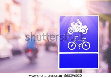 Motorcycle and bicycle keep left lane warning sign on blur traffic road with colorful bokeh light abstract background. Copy space of transportation and travel concept. Retro tone filter color style.