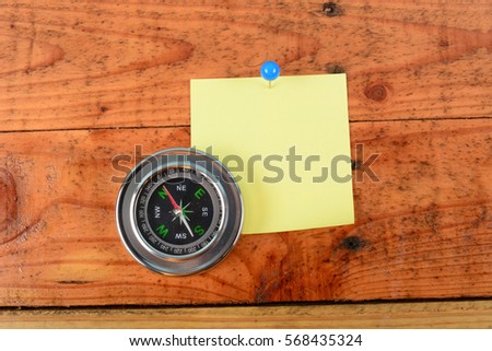 Blank yellow Notepad with a pin and compass. Wooden background