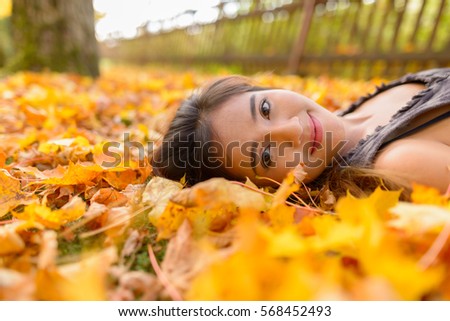 Young beautiful Asian woman lying down on yellow autumn leaves