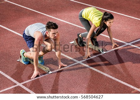 Male and female athlete in starting position at starting block of cinder track Royalty-Free Stock Photo #568504627