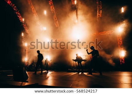 Band Silhouette. Сoncert of popular group.  Rock band performs on stage. Guitarist, bass guitar, keyboard player and drums. Bright light show at the stadium. 