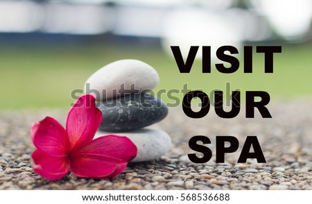 Spa concept of zen stones with deep red plumeria flower. Word visit our spa.