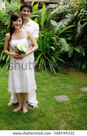 Couple in garden, man with arms around woman, woman holding bouquet