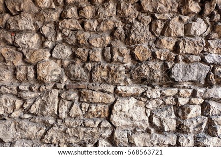 Stone wall - stacked stone blocks / cobblestone in a wall, each rock has a different shape and size, creating an unique pattern or texture. The surface of the stones is rough and the gaps are shady.