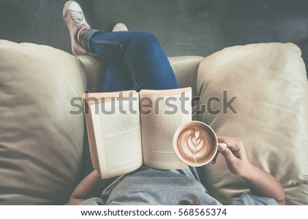 Soft photo of young girl reading a book and drinking coffee, top view Royalty-Free Stock Photo #568565374