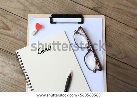 Goals - simple concept of text on notebook, clipboard, pen and glasses on wooden table. top view