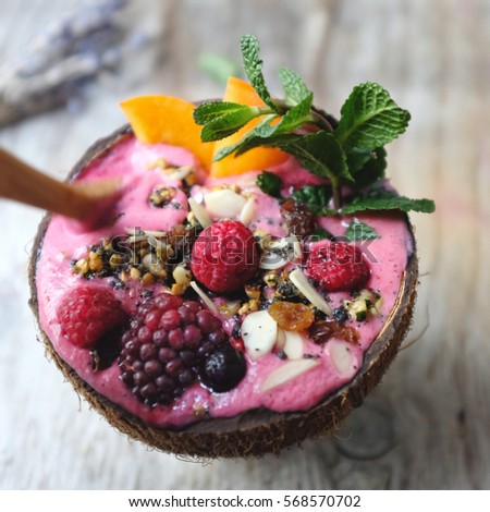Mixed berries smoothie in almond milk with dates, grounded grilled black sesame, chia seed and banana. Topped with berries, persimmon, almond, black sesame, granola. Serve in coconut bowl. Royalty-Free Stock Photo #568570702