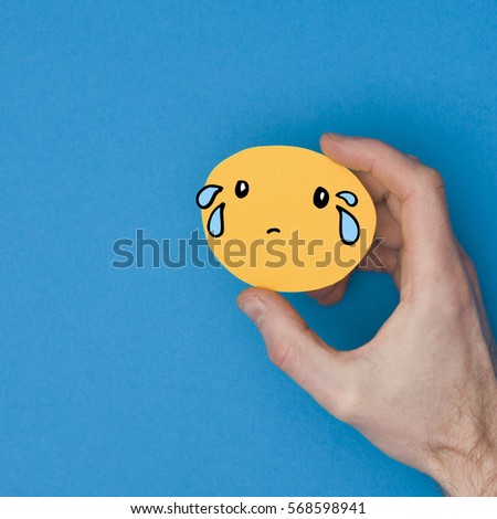 Sad emoji. Male hand holding a yellow emotion face with a hand drawn expression