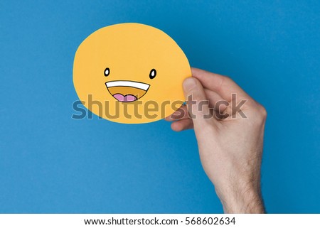 Happy smiling emoji. Male hand holding a yellow emotion face with a hand drawn expression