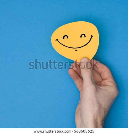 Smiling emoji. Male hand holding a yellow emotion face with a hand drawn expression
