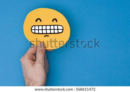 Happy grinning emoji. Male hand holding a yellow emotion face with a hand drawn expression