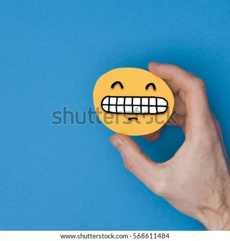 Happy grinning emoji. Male hand holding a yellow emotion face with a hand drawn expression
