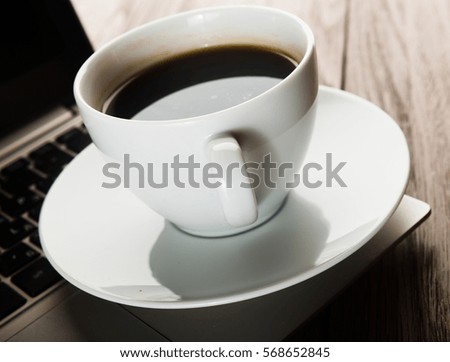 Cup of coffee and laptop on wooden table.

