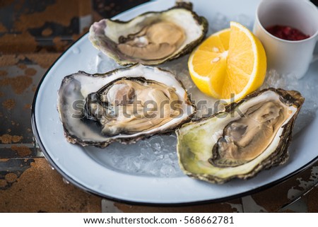 Oysters on a white plate - tasty and healthy. Seafood close-up on a dark background. Royalty-Free Stock Photo #568662781