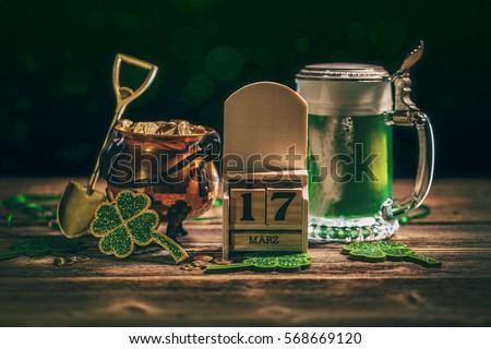 Block calendar for St Patrick's Day, March 17, with green beer and pot of gold, on wooden background.