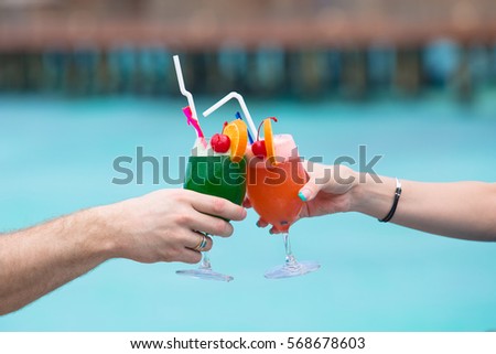 Couple with colorful cocktails on the background of turquoise water.