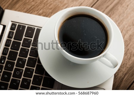 Cup of coffee and laptop on wooden table.

