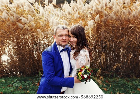 Groom in bright blue suit holds bride tender while they pose before the reed