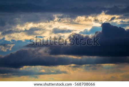 Stormy sky with rays of sunlight. Bight sunset with rainy clouds. Tropical sunset romantic photo background. Fluffy clouds with sun reflections. Orange sunlight on grey clouds. Rainy season weather