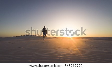 Back view silhouette of a runner man running along on the beach at sunset with sun in the background. Vintage effect style pictures.