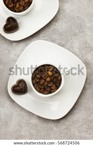 White cups for espresso filled with coffee beans and chocolate in form of heart on a light background. Top view. Toning.
