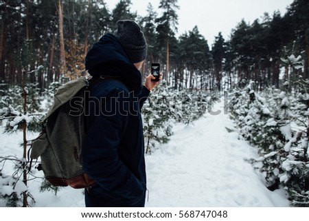 Traveler takes selfie of snowy landscape in winter forest on mobile phone