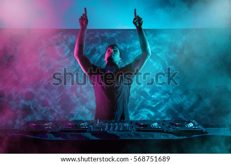 Charismatic disc jockey at the turntable. DJ plays on the best, famous CD players at nightclub during party. EDM, party concept. Royalty-Free Stock Photo #568751689