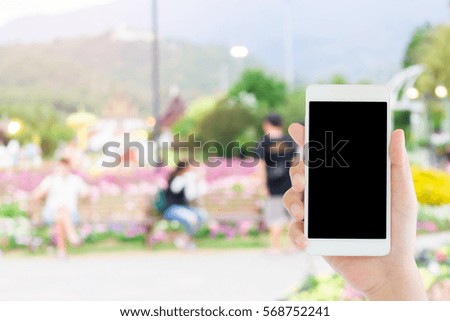 woman use mobile phone and blurred image of people in the park in the evening with a lot of trees and colorful flowers