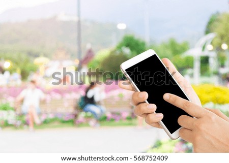 woman use mobile phone and blurred image of people in the park in the evening with a lot of trees and colorful flowers