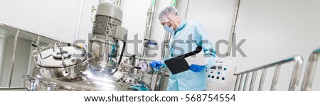 wide-screen picture, scientist in blue lab suit and gas mask working with control panel, look at steel tank, check readings Royalty-Free Stock Photo #568754554