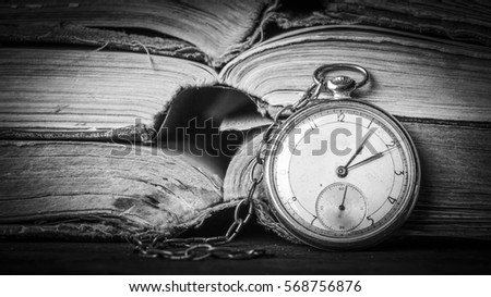 Decaying clock on the background of old shabby wise books. Black and White photograph