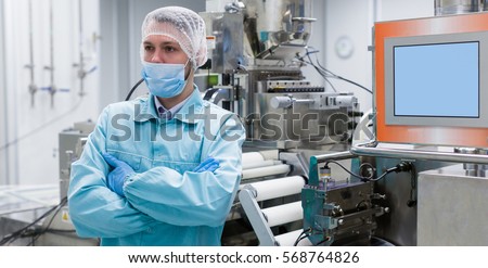 wide-screen, picture of scientist with crossed hands in lab suit standing near steel machine with shafts