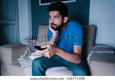 Bored man watching tv on the couch at night Royalty-Free Stock Photo #568771408