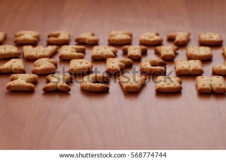 Letters of salty crackers lay on a wooden brown surface in the order similar to the layout of the buttons on the computer keyboard. Funny imitation of the keyboard using cookies
