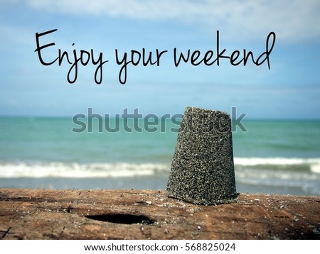 Holiday concept photo with a view of a cup of beach sand on top of driftwood and sea background with message of "Enjoy your weekend". 