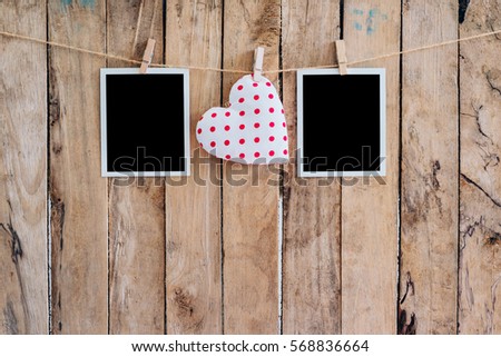 White heart and two photo frame hanging on clothesline rope with wooden background.