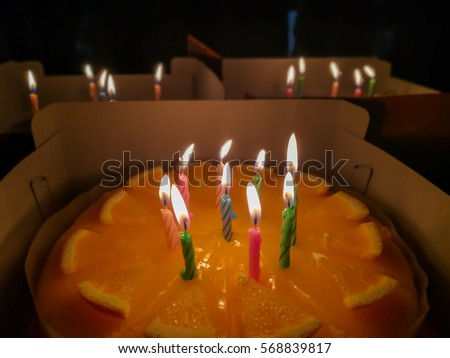 Selective focus at middle candle on orange cake. Happy birthday celebration event, light from little candles in dark room. Surpise occasion for somene lover.