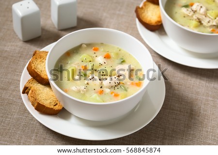 Chicken and potato chowder soup with green bell pepper and carrot in bowls with toasted bread slices on the side, photographed with natural light (Selective Focus, Focus one third into the first soup) Royalty-Free Stock Photo #568845874