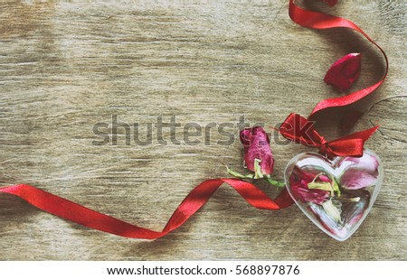 Valentine's Day composition with dried roses, ribbon, transparent heart box on wooden board, retro toned effect. 
