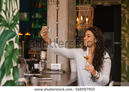 Attractive woman taking self portrait by mobile phone while holding a glass of wine