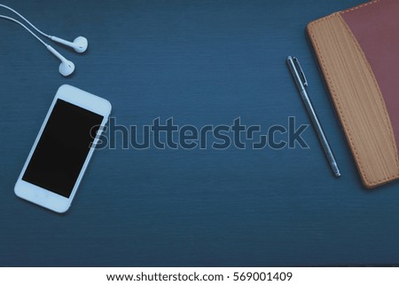 Dark wooden background with gadgets,smart phone, pen ,Notebook, and headset.selective focus.lowkeylight.
