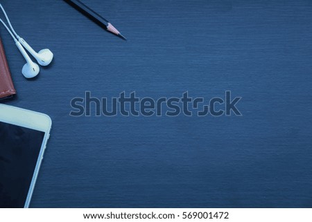 Dark wooden background with gadgets,smart phone, Pencil,Notebook,and headset.selective focus.lowkeylight.