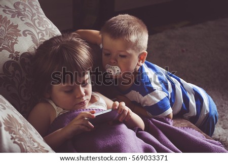Little cute sister and brother is looking or playing with a smart phone at home